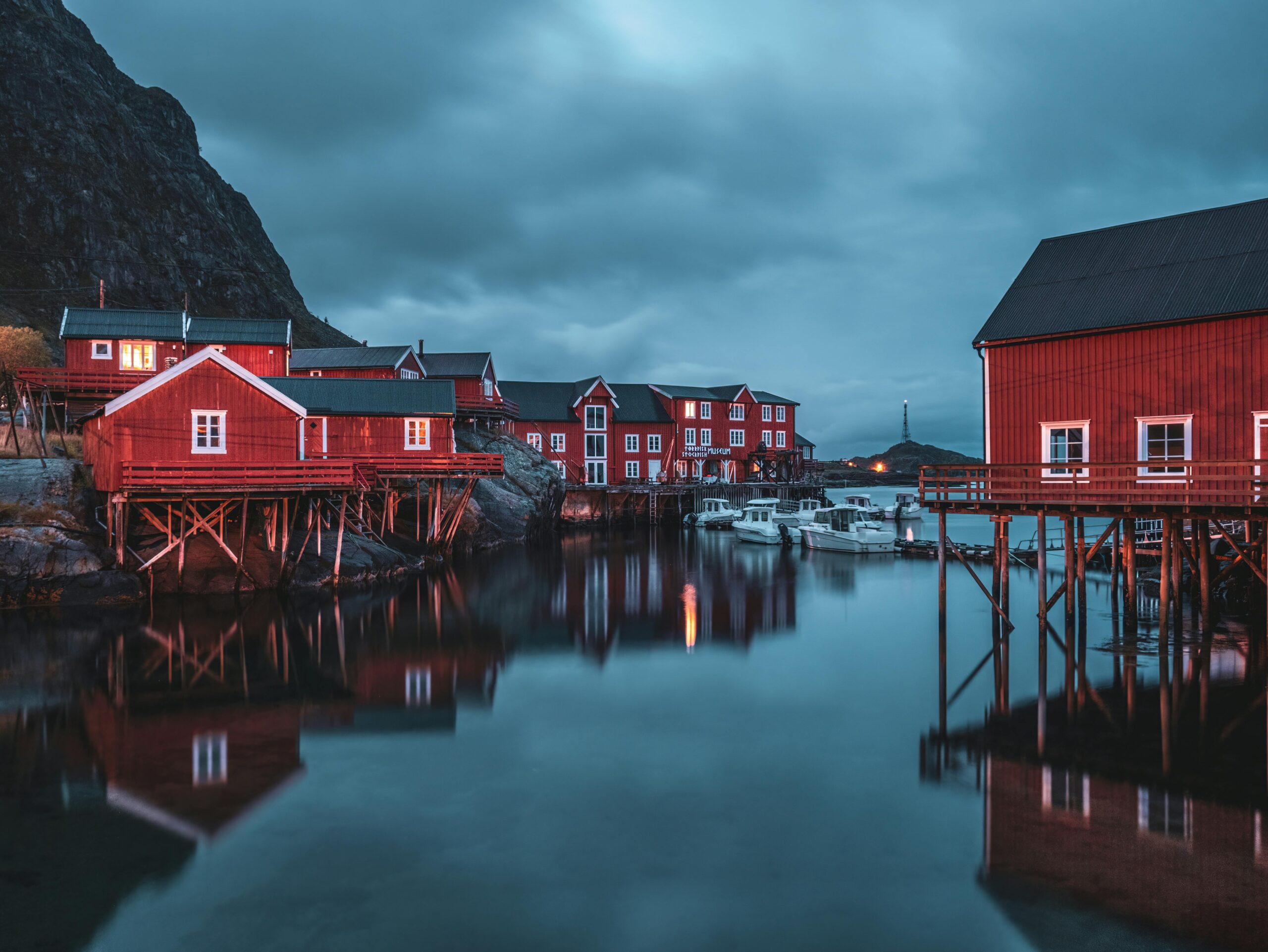 Stunning view of red stilt houses reflecting in the water at Å i Lofoten during twilight.