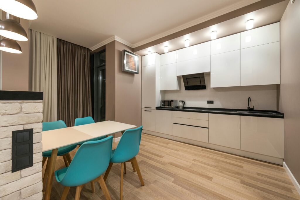 Interior of design of spacious furnished kitchen with beige walls and laminated floor and dining zone with wooden table and blue chairs